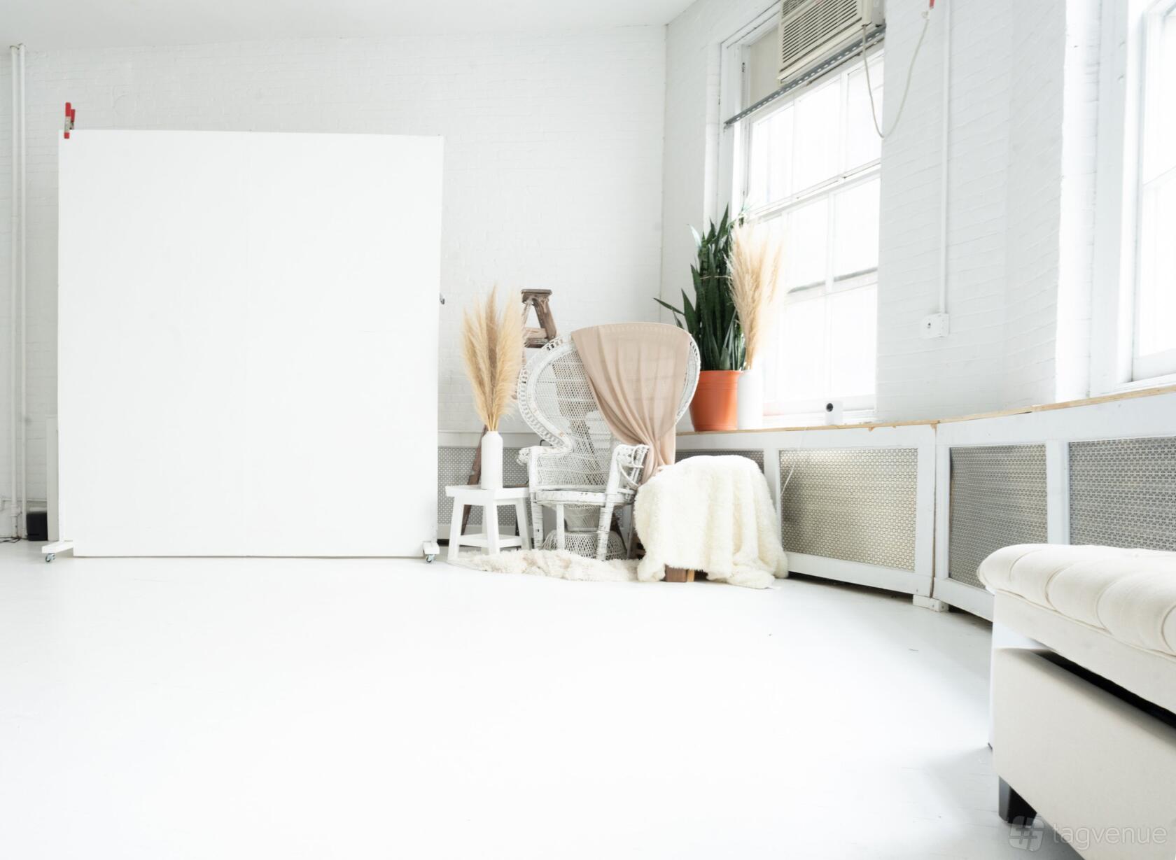 A photo studio with white floors, large windows, wicker chairs, pampas grass, and neutral decor at LeVue Studios.