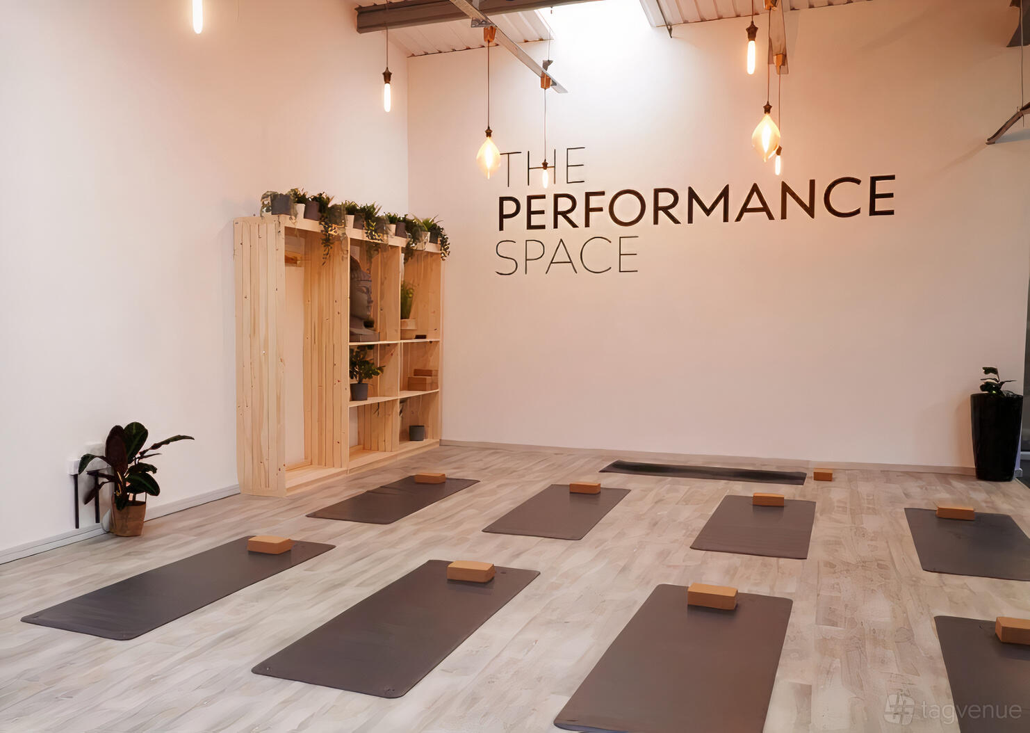 A fitness studio with yoga mats and blocks on light wood floors beneath pendant lights at The Performance Space.