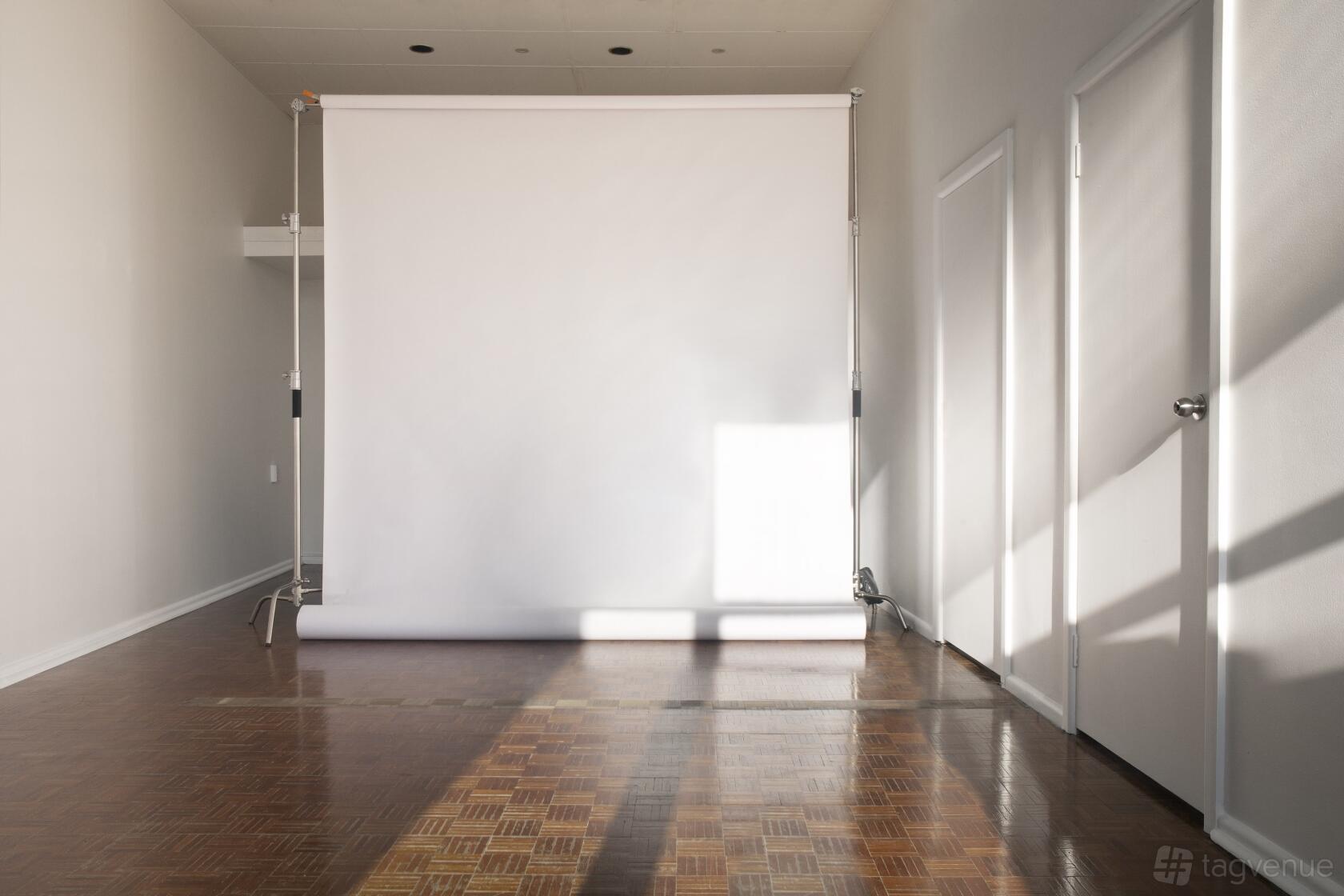 A photo studio with a seamless white backdrop, parquet flooring, and natural light at Cielo Studio.