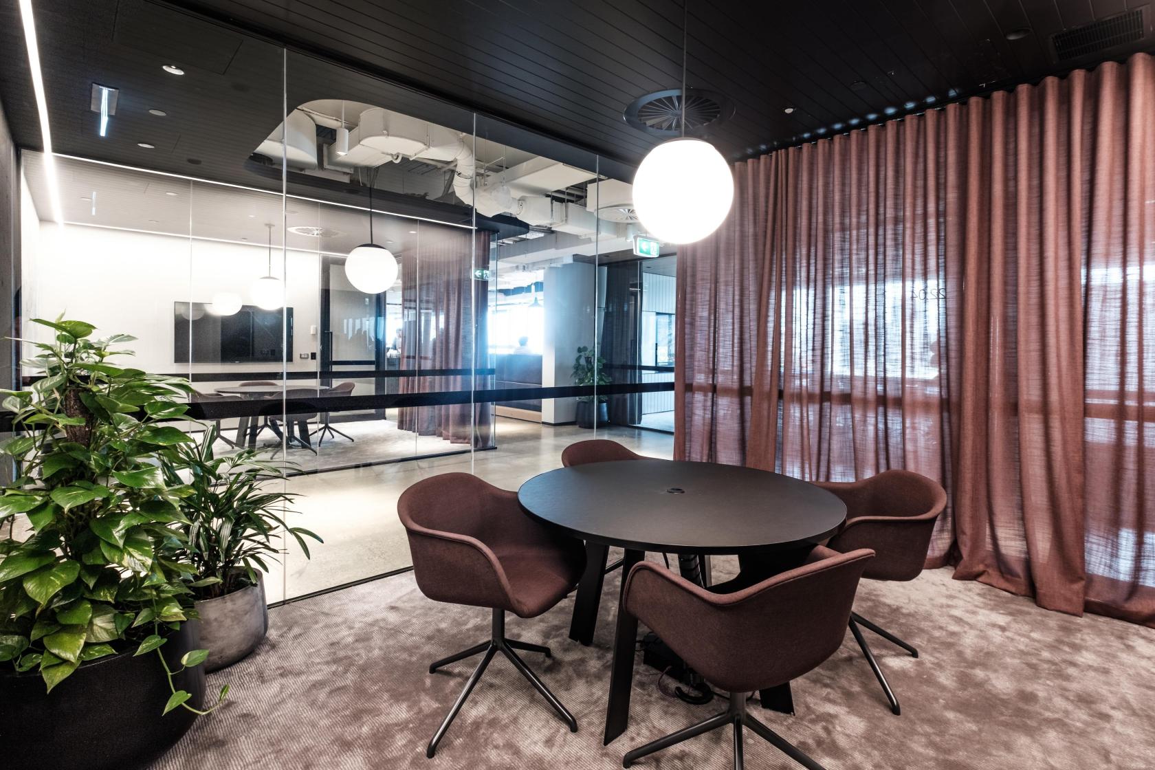 A meeting room with a round table, four upholstered chairs, floor-to-ceiling curtains, and glass walls at Space&Co. 8 Exhibition Street, Melbourne.