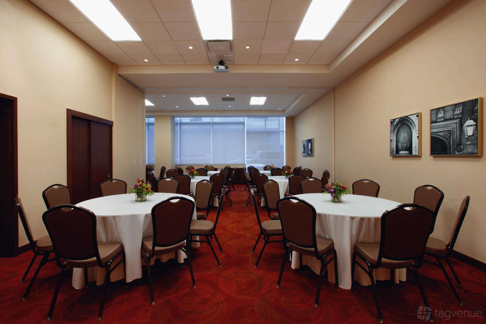 A hotel meeting room with round tables covered in white linens, brown chairs, and large windows at Hyatt Place Chicago South.