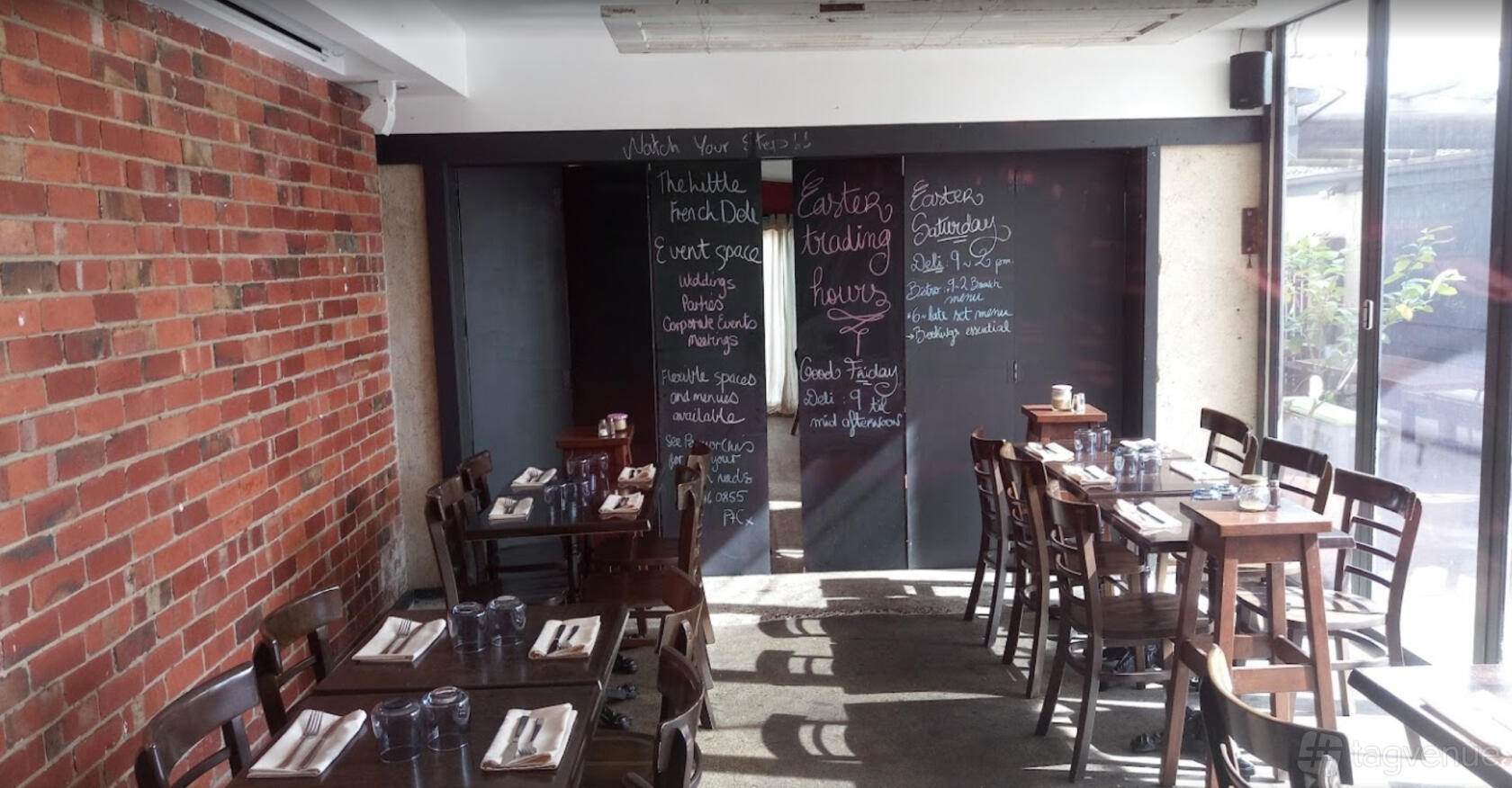 A restaurant with exposed brick walls, chalkboard menus, wooden tables, and natural lighting at The Little French Deli & Bistro.