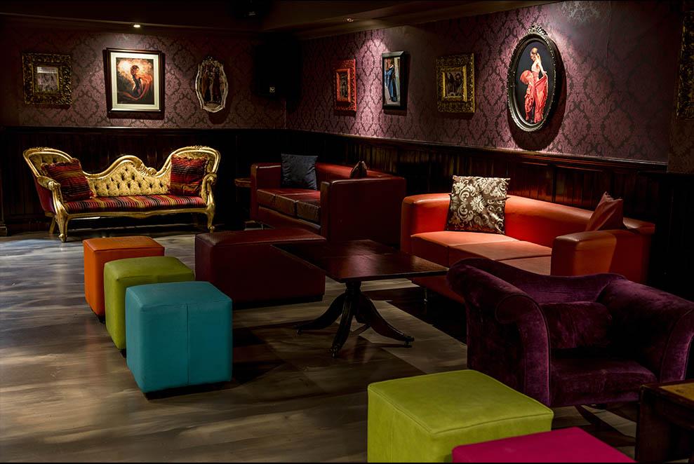 A function room with vintage decor, colorful velvet seating, and framed artwork on patterned walls at Zingara.