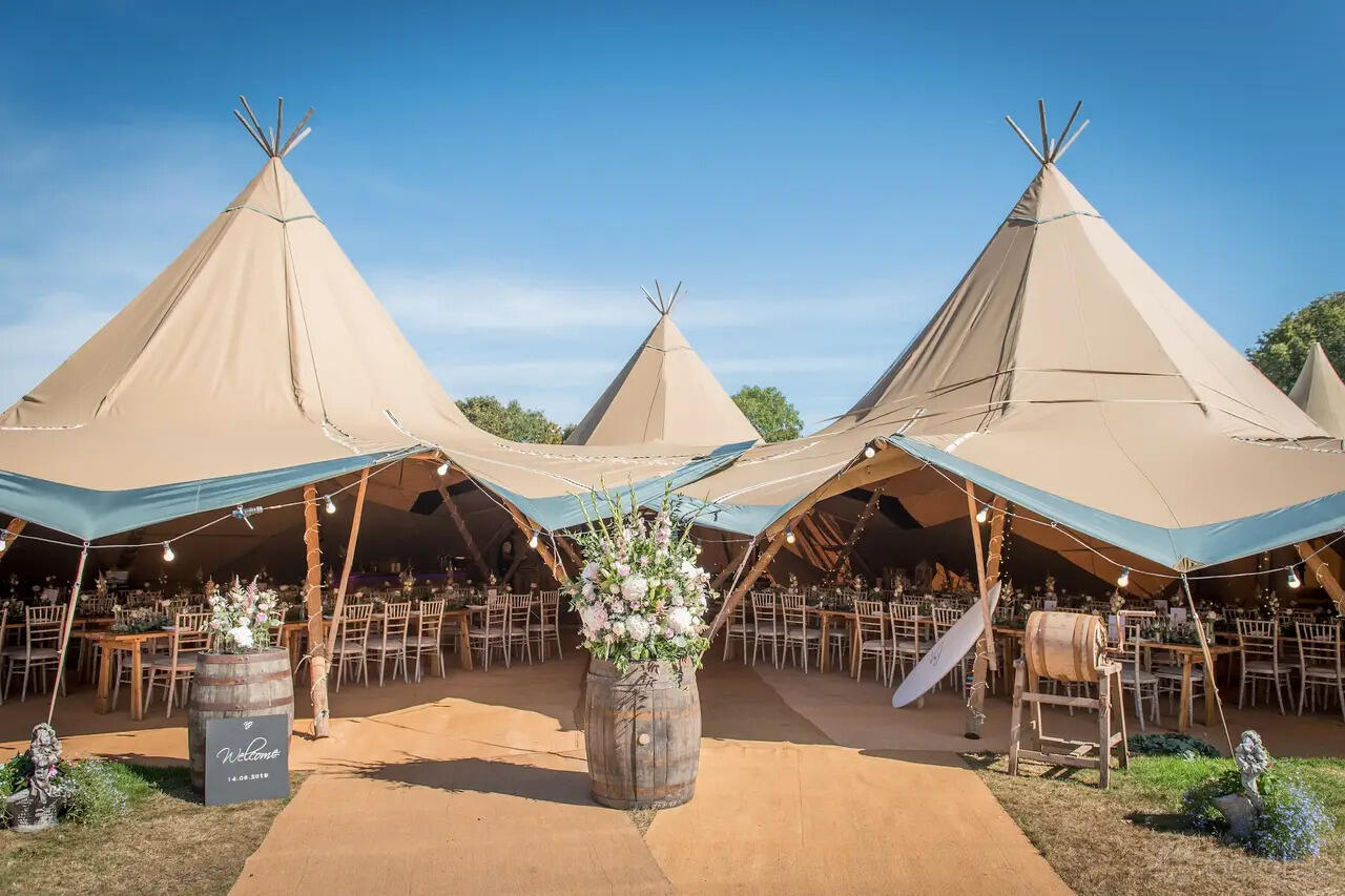 An outdoor hall with tipi-style tents, string lights, and banquet seating at Beaumont Hall.