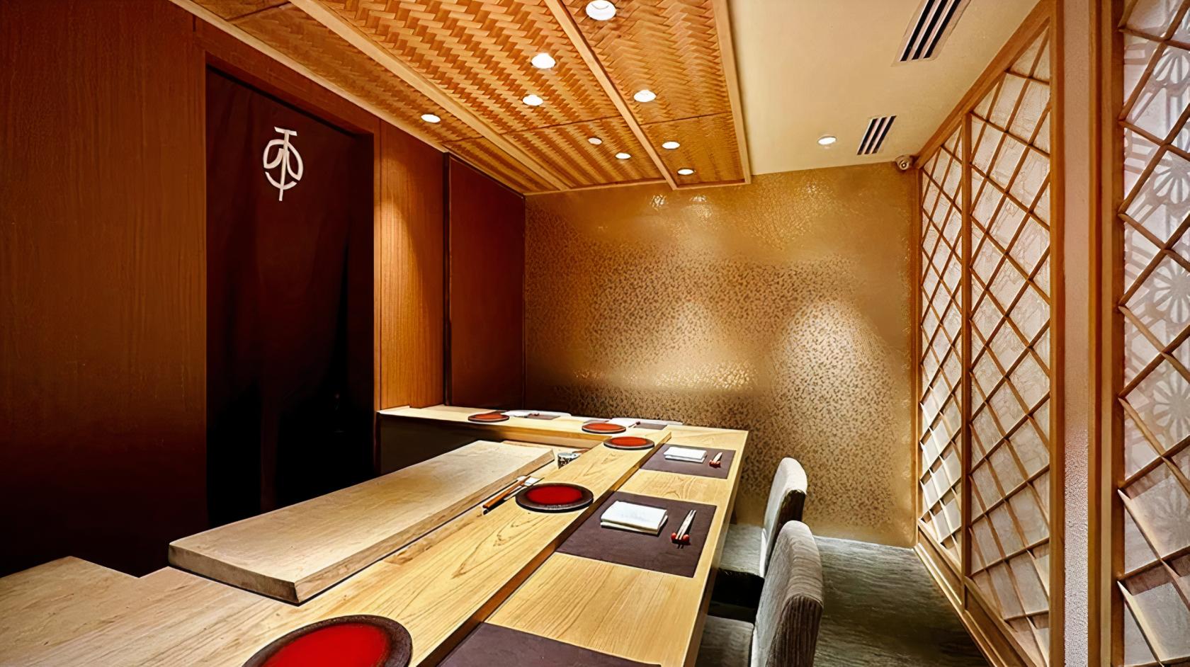 A restaurant with a wooden sushi counter, textured walls, and woven ceiling panels at Shoukouwa Restaurant.