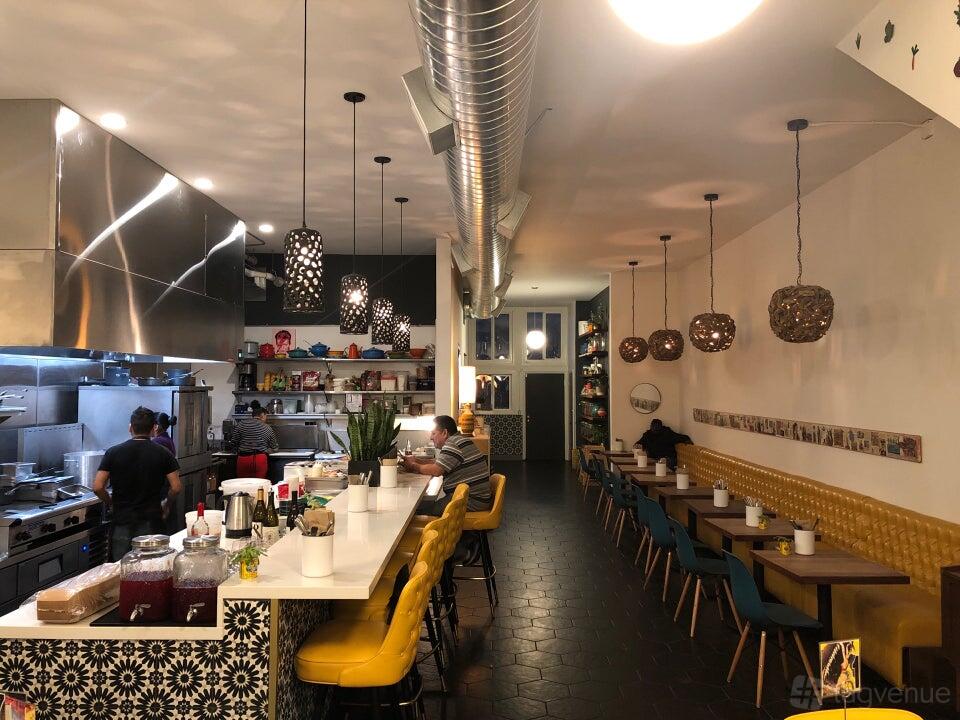 A restaurant with an open kitchen, patterned tile counter, and yellow tufted banquette seating at Tato.