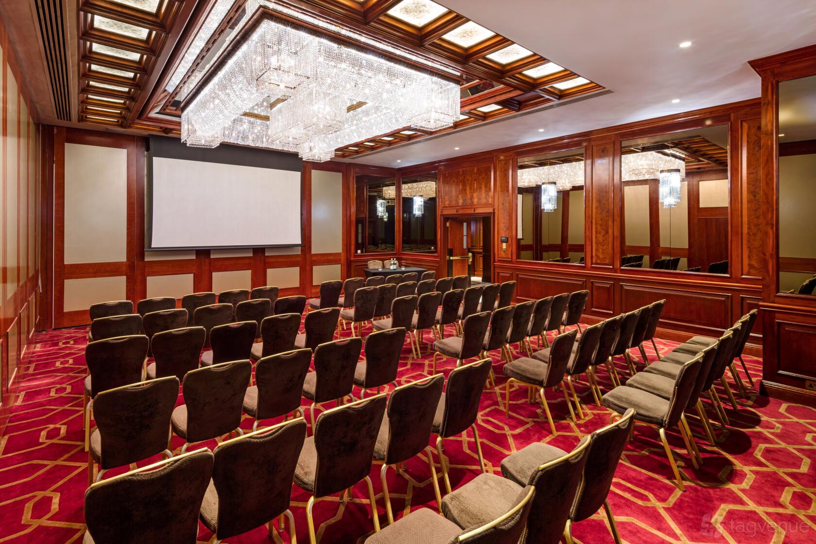 An event space with red patterned carpet, rows of chairs, wood-paneled walls, and crystal chandeliers at Radisson Blu Hotel, London Heathrow.
