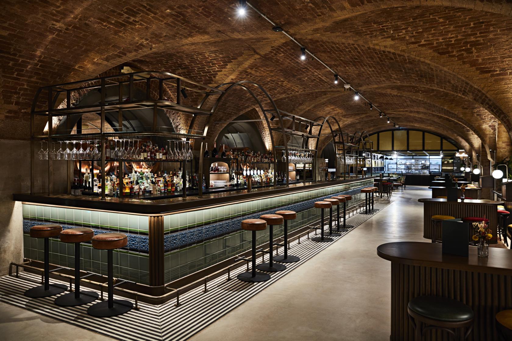 An event space in a restaurant with exposed brick arched ceilings, a long tiled bar, and high stools at The Libertine.