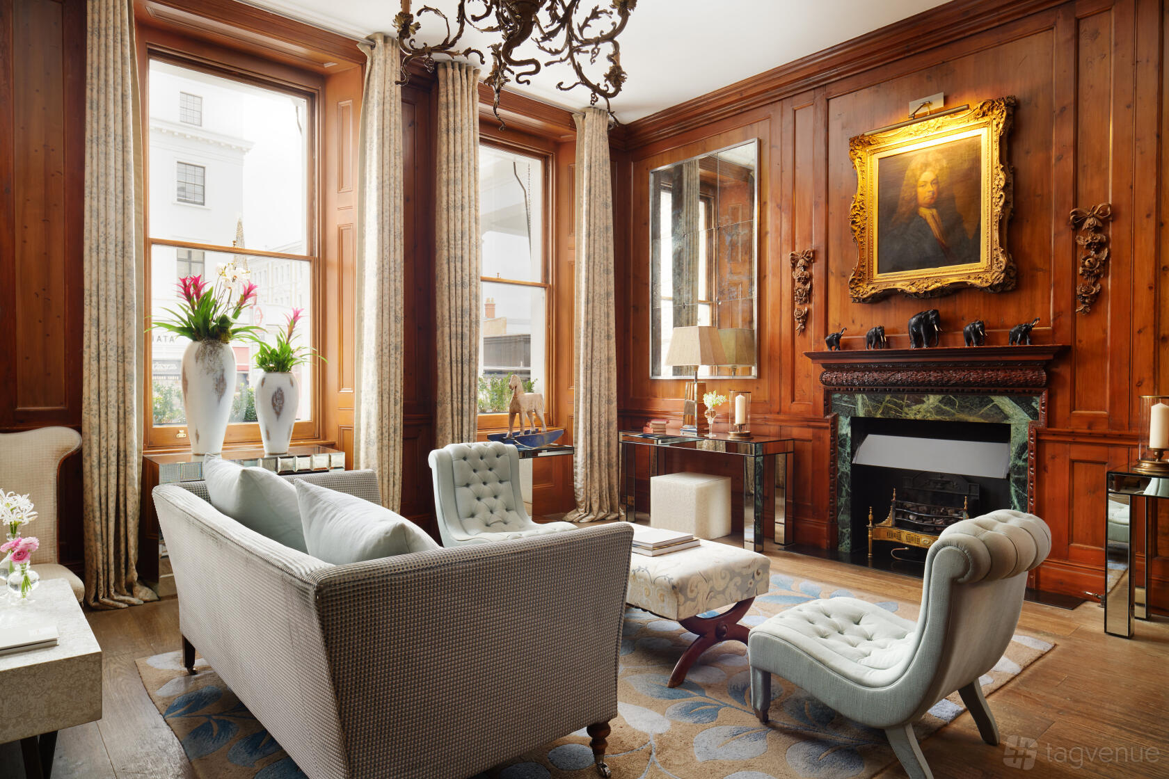 A hotel meeting room with wood-paneled walls, large windows, and elegant seating around a fireplace at The Pelham Hotel.