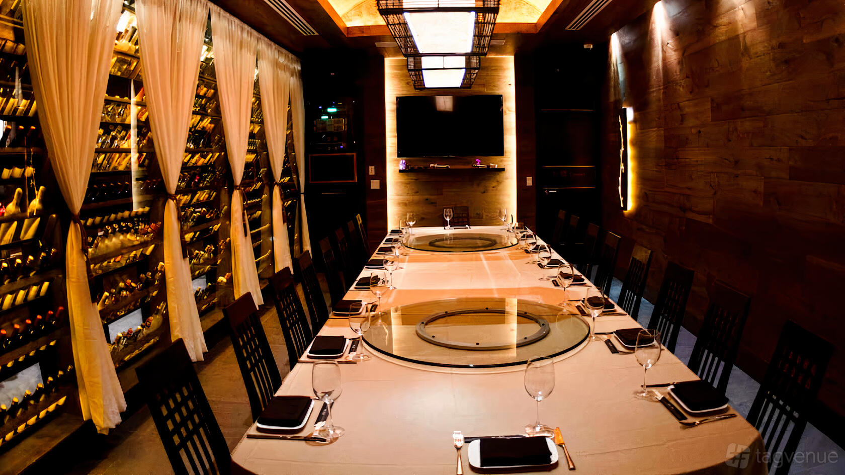 A private dining room with a long table set with glassware, wine wall, and a large TV at MoCA Asian Bistro - Queens.