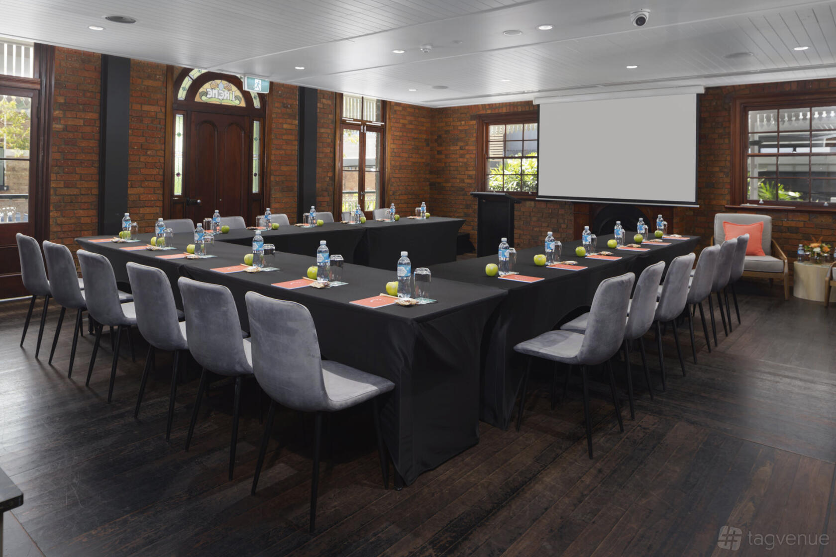 An event space in a hotel with exposed brick walls, U-shaped tables with black linens, and floor-to-ceiling windows at Kennigo Hotel Brisbane.