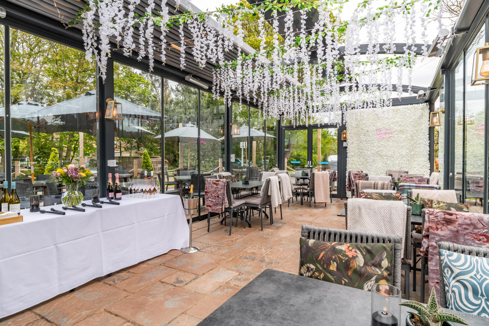 An event space in a bar with glass walls, floral ceiling garlands, and patio seating at The Fishery Inn.