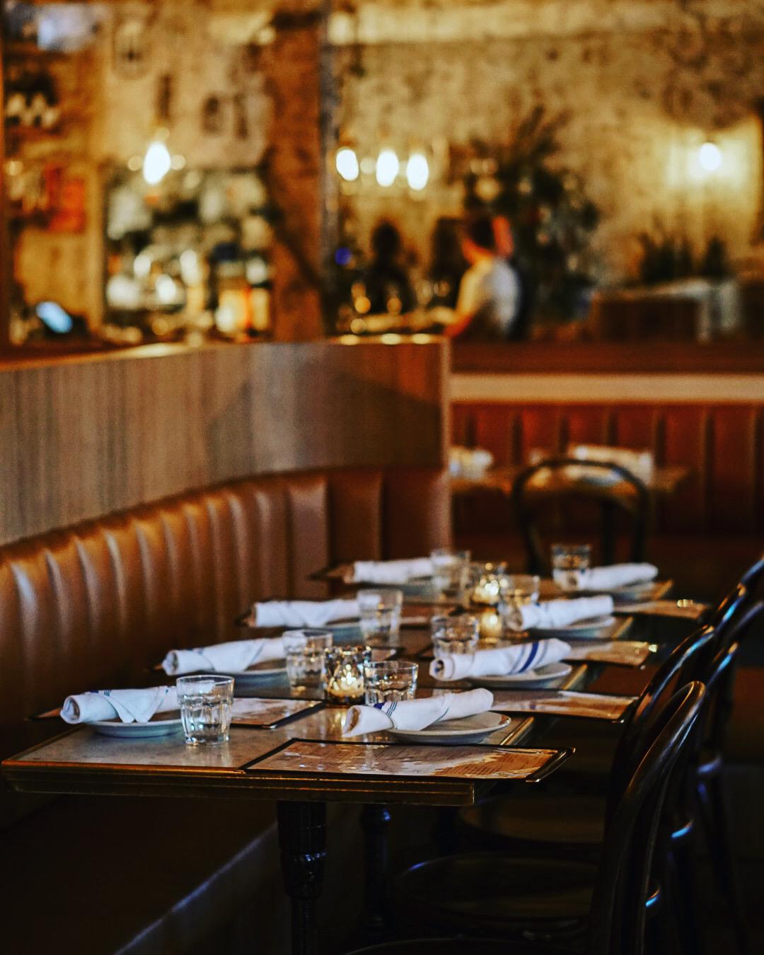 A restaurant with leather banquettes, wooden tables set with white napkins and glassware at Mino Brasserie.