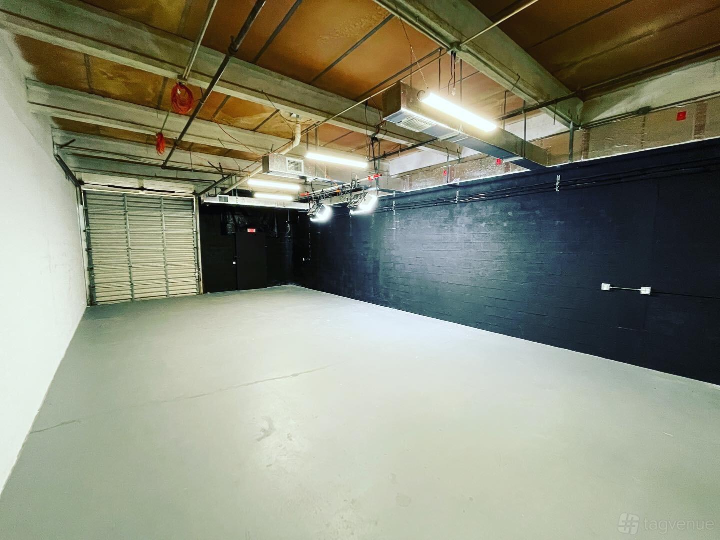 A photo studio with a black accent wall, exposed ceiling beams, and overhead fluorescent lighting at Bridges Productions LLC.