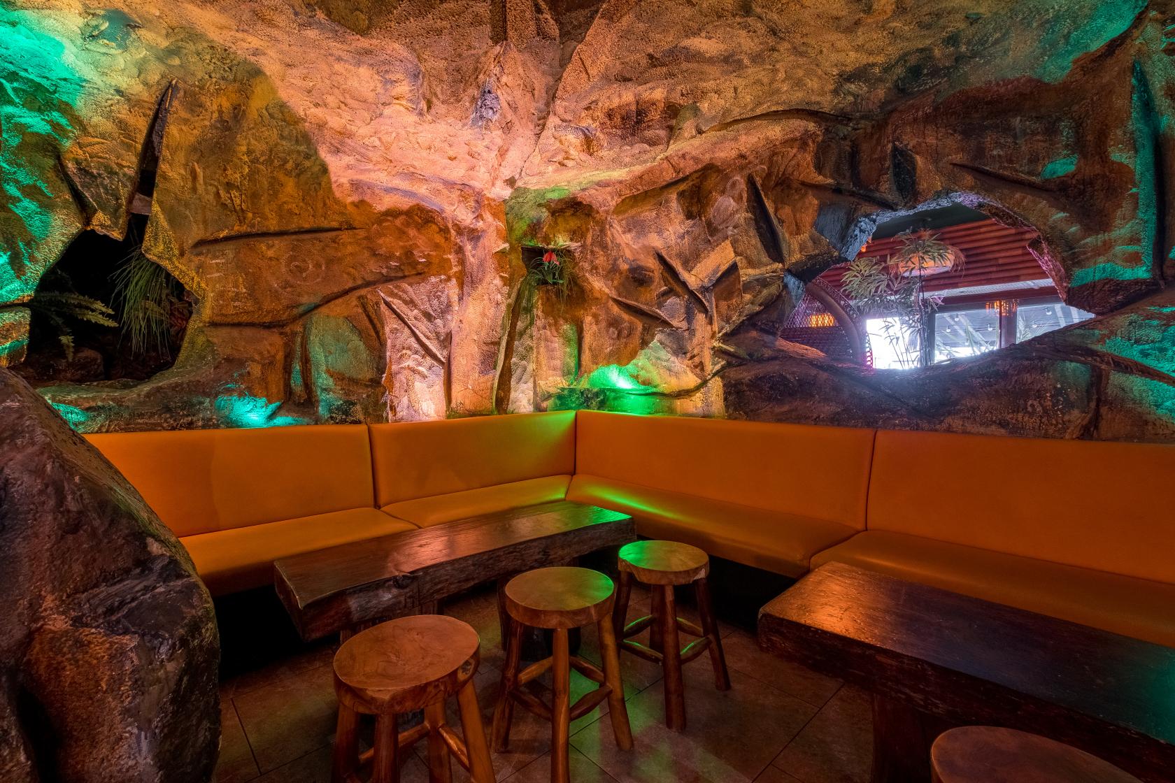 An event space with cave-like rock walls, yellow banquette seating, and wooden tables at Sugar Cane.