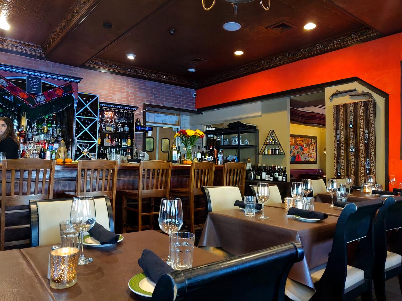 A restaurant with a wooden bar, wine racks, and tables set with glasses and napkins at Bistro Aracosia.
