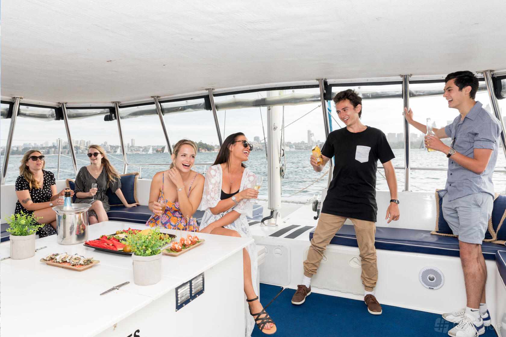 A boat with open seating, panoramic harbour views, and a table set with snacks aboard Sea Sydney Harbour.
