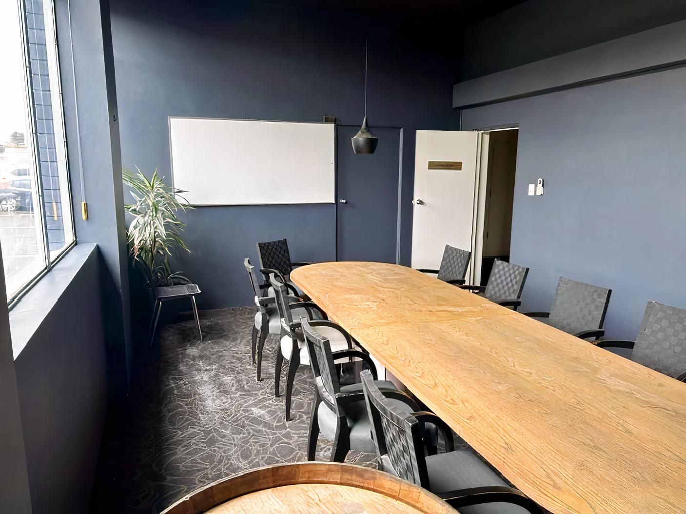 A boardroom with a long wooden meeting table, black chairs, a whiteboard, and large window at Berowra RSL Club.