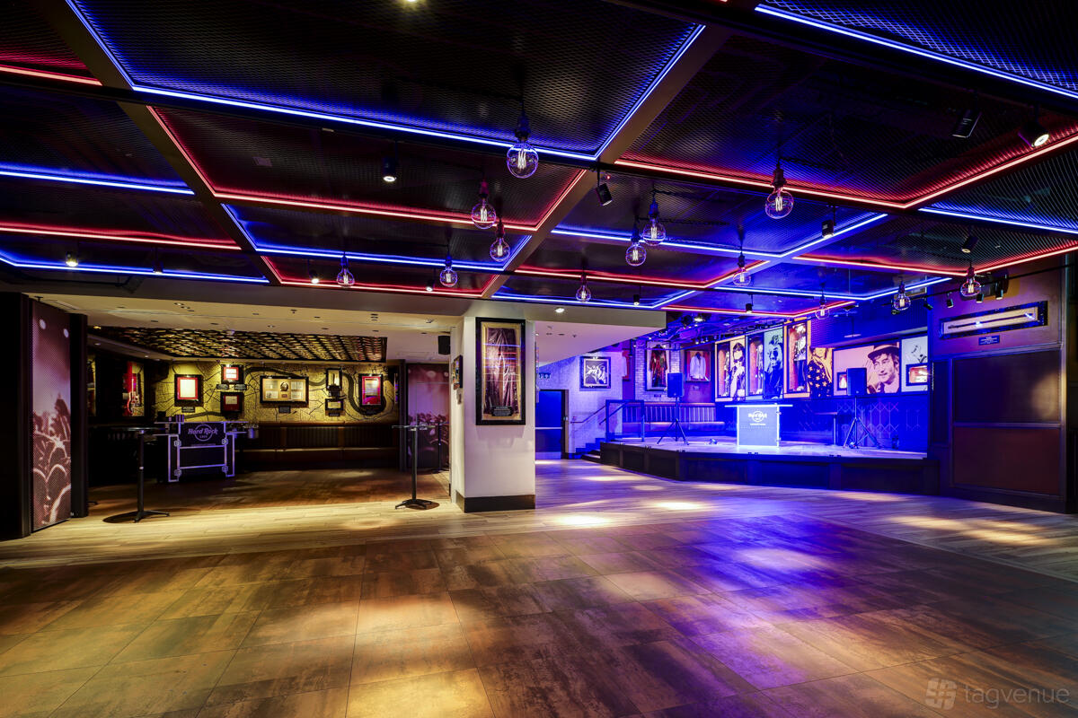 An event space with neon ceiling lights, wood floors, framed music memorabilia, and a small stage at Hard Rock Cafe Piccadilly Circus.