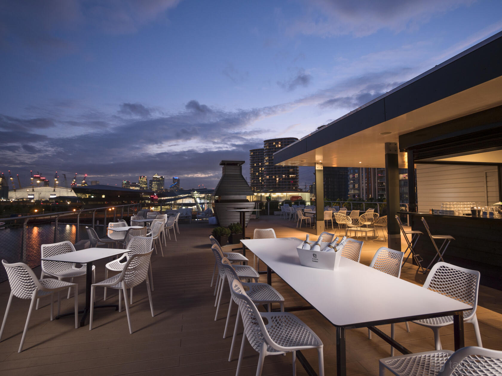 A rooftop terrace with white outdoor tables and chairs overlooking the city skyline at Good Hotel London.