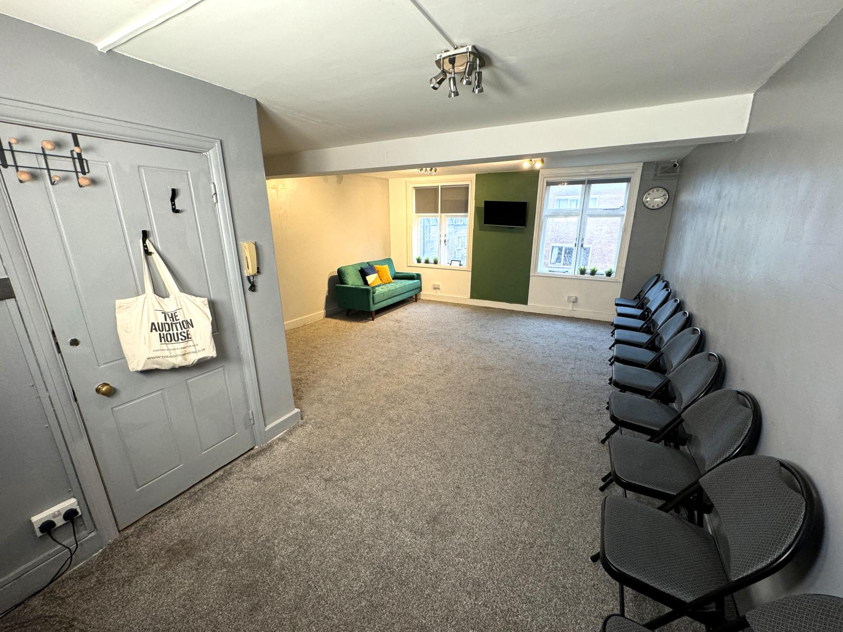 A rehearsal studio with gray carpet, folding chairs along the wall, and a green sofa at The Audition House 3x studios.