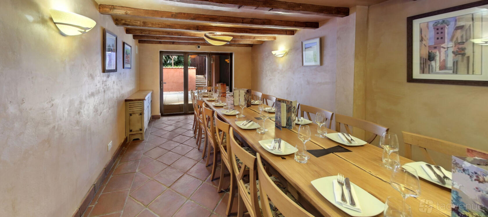 A dining room with a long wooden table, wooden chairs, beamed ceiling, and terracotta tile floor at Stuzzichini.