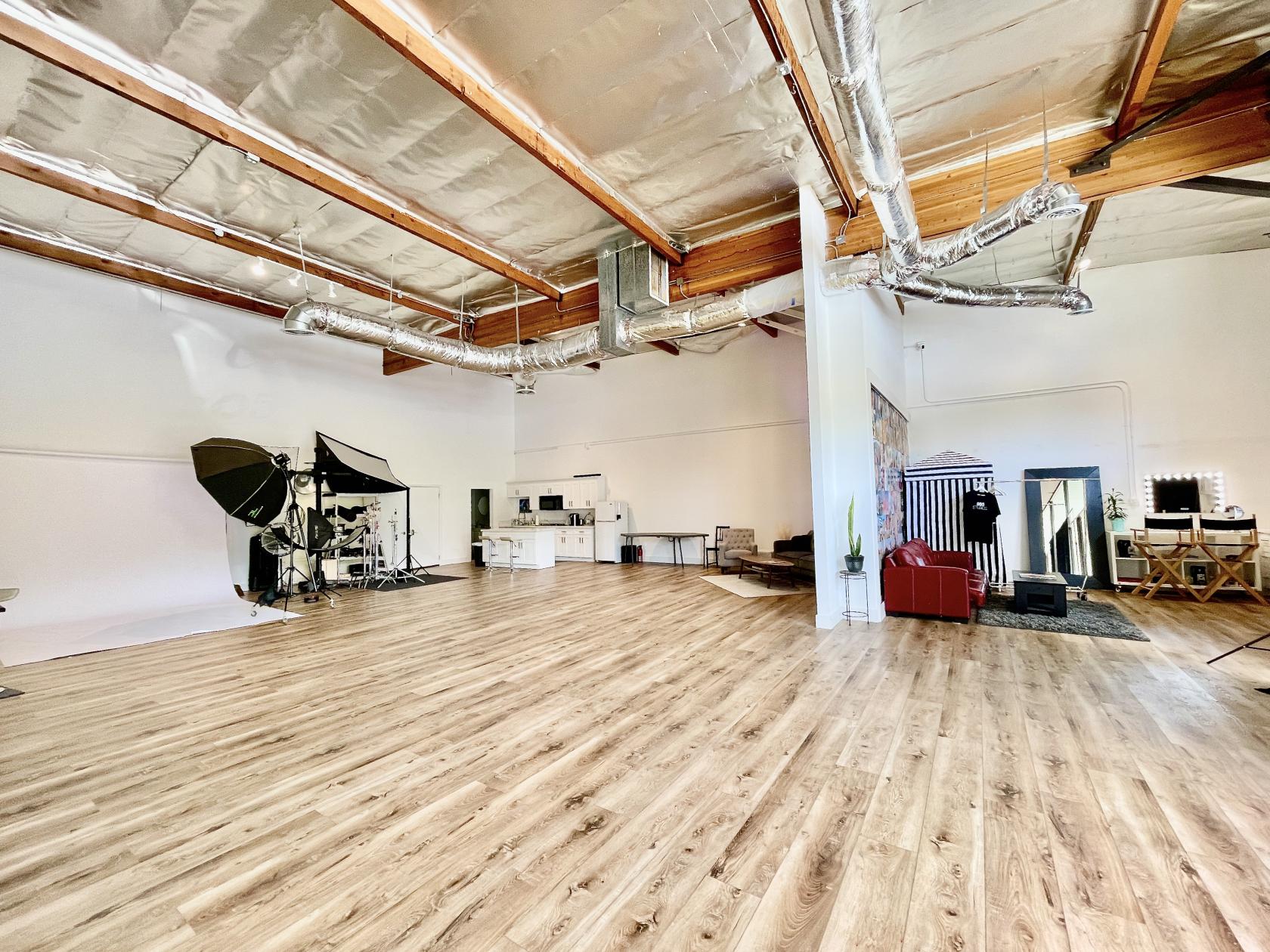 A photo studio with wood floors, vaulted ceilings, exposed ducts, a kitchenette, and studio lighting at 805 Studios.