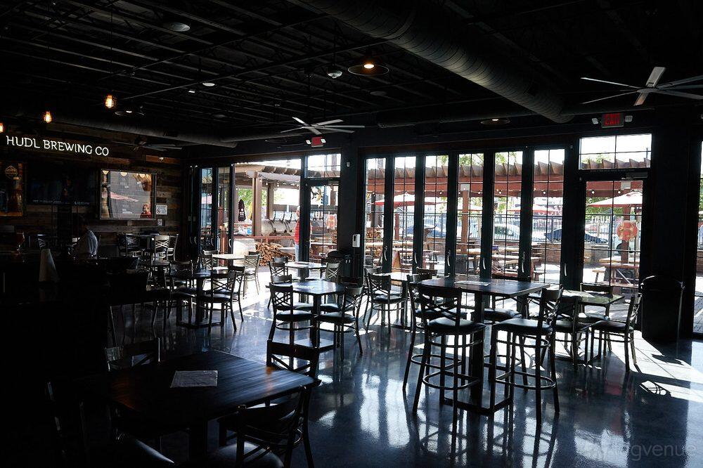 A bar with glass garage doors, polished concrete floors, and wooden tables at HUDL Brewing Company.