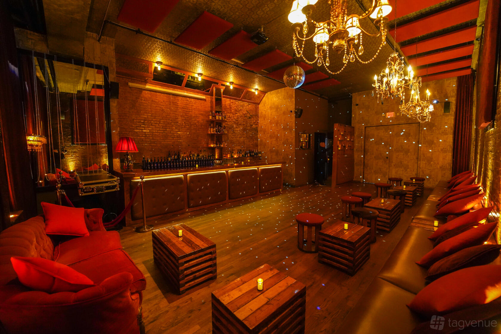 A function room in a bar with exposed brick walls, chandeliers, and wooden tables at Velvet Brooklyn.