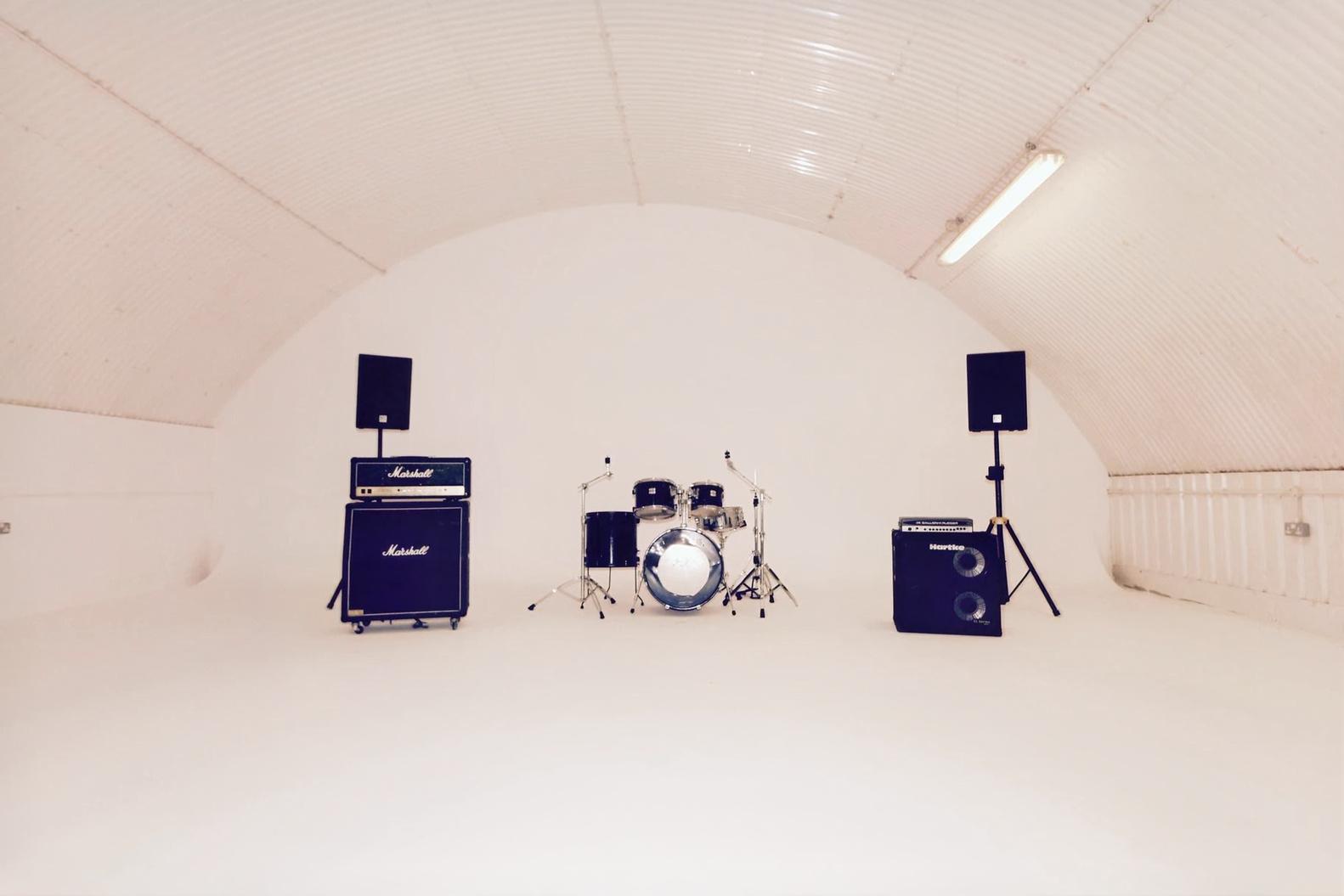 A photo studio with curved white walls, high ceiling, and a drum set with amplifiers at The Blue Studios.