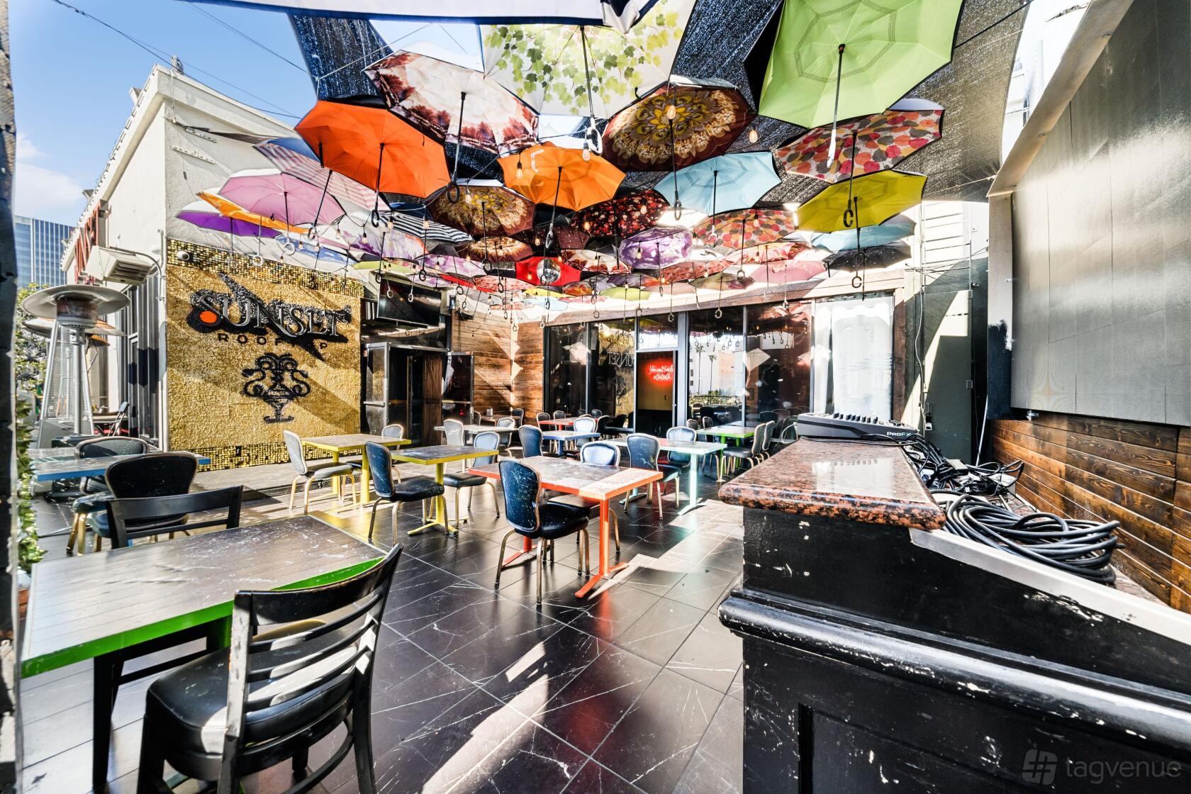 An outdoor terrace with colorful umbrellas suspended overhead and mixed seating at Sunset Rooftop.
