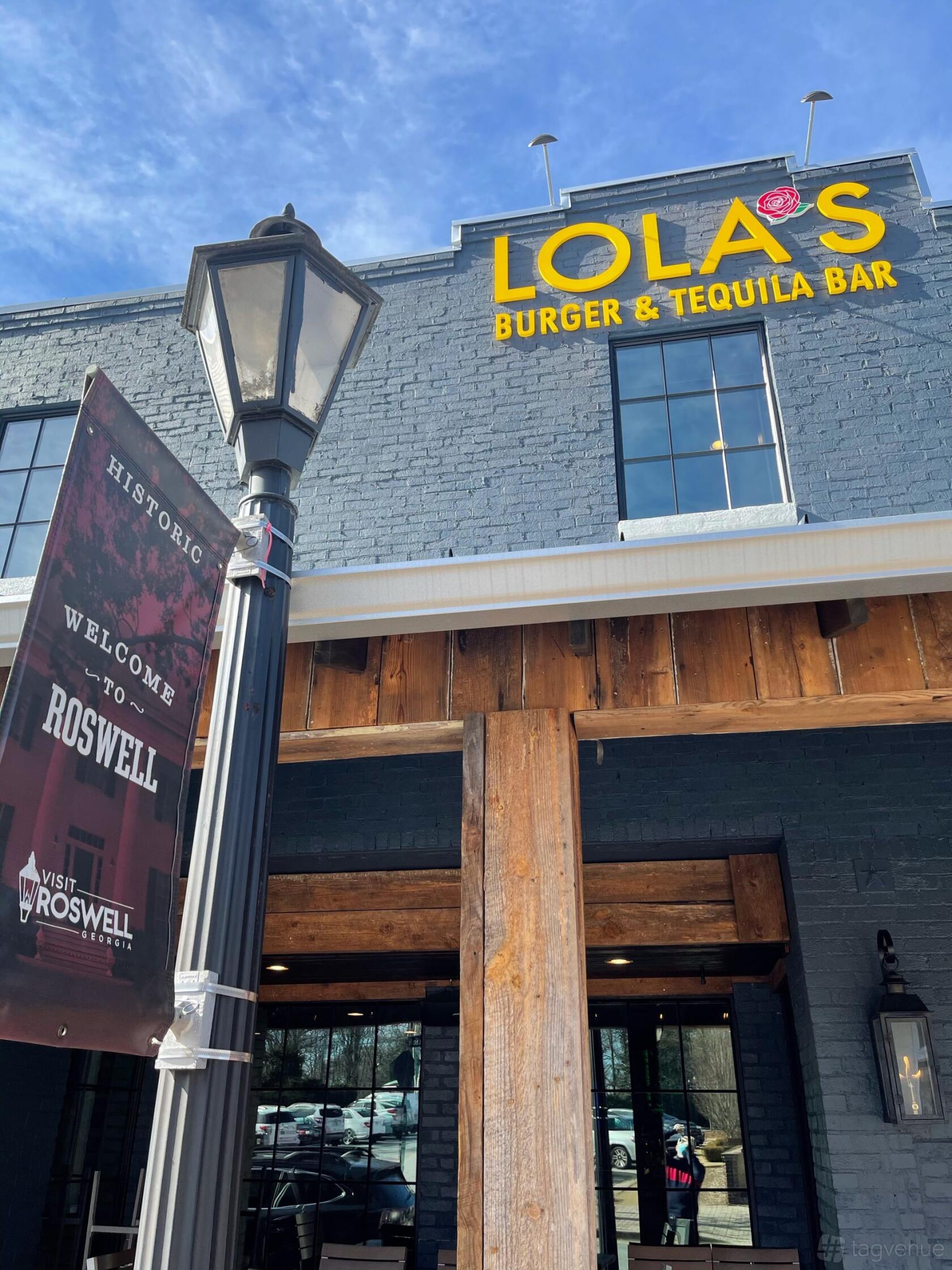 A restaurant with a rustic wooden entrance and navy brick facade at Lola's Burger & Tequila Bar.