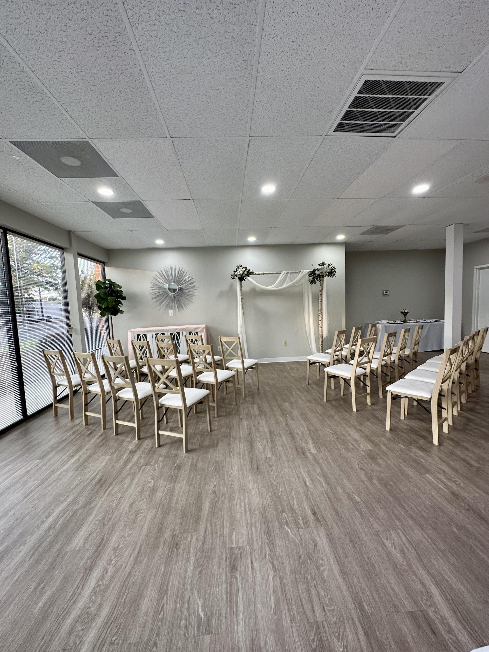 An event venue with wood flooring, rows of light wood chairs, and a simple wedding arch at Fruitful Flex Space.