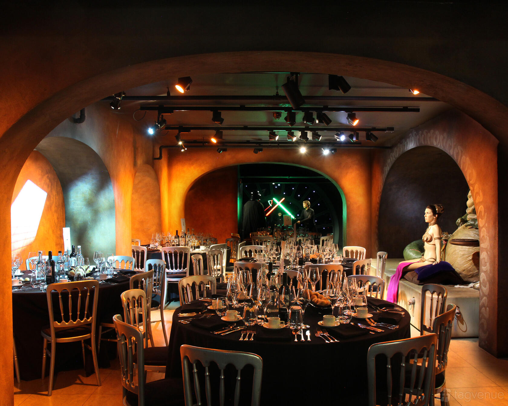 An event space with arched alcoves, round tables set with glassware, and a wax figure at Madame Tussauds.