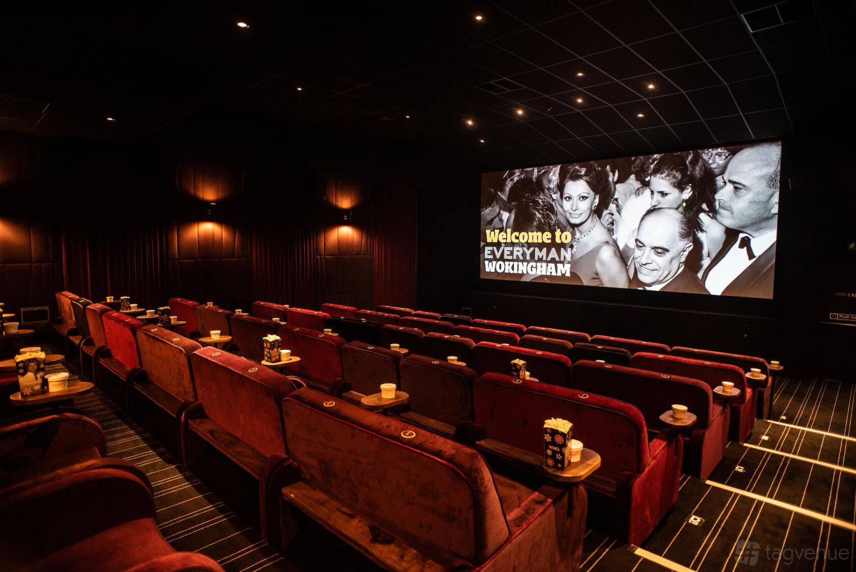 An auditorium with red velvet sofas, side tables, and a large cinema screen at Everyman Wokingham.