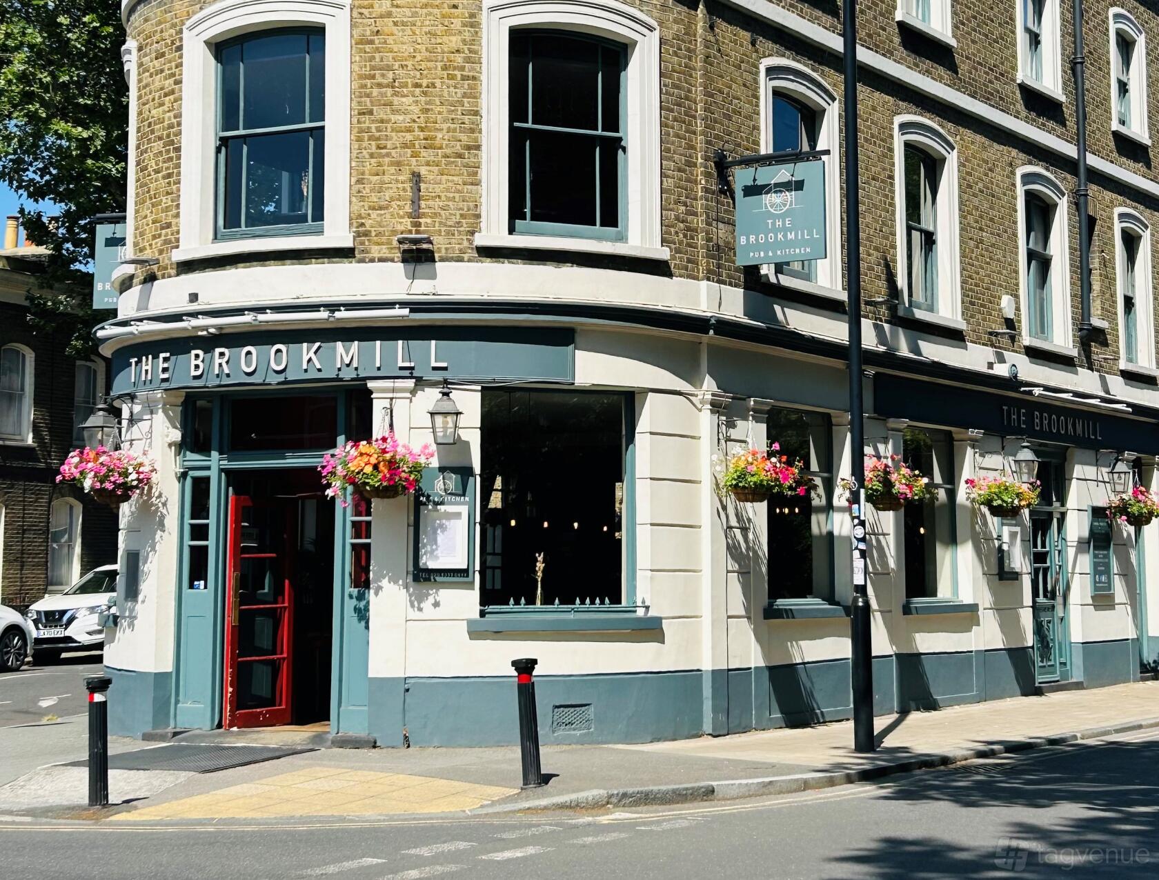 A corner pub with hanging flower baskets, large windows, and a blue facade at The Brookmill.