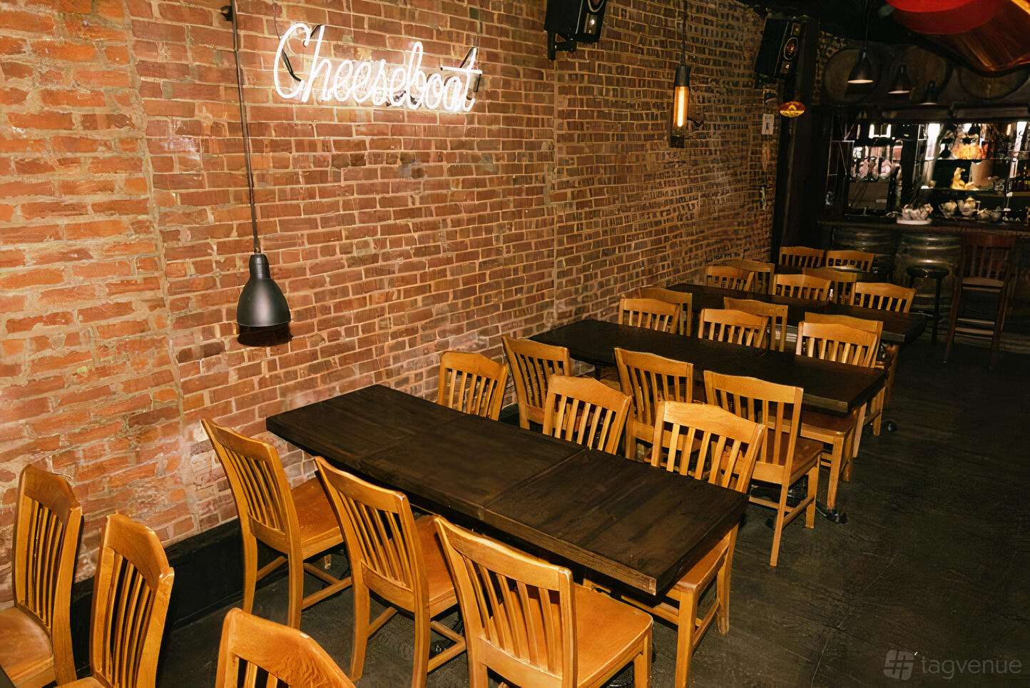A restaurant dining area with exposed brick walls, wooden tables and chairs, and a neon Cheeseboat sign at Cheeseboat Manhattan.
