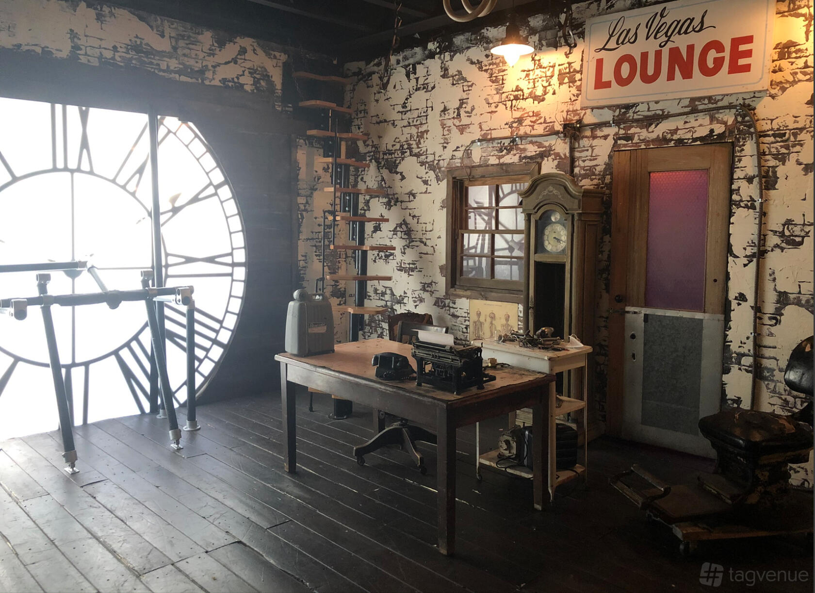 A photo studio with a giant clock face window, vintage desk, and brick walls at Photo Bang Bang.