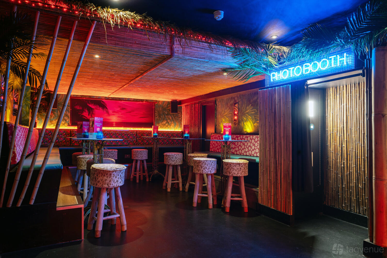 A tropical-themed event space with bamboo decor, tiki bar stools, and neon signage at Tiki Hideaway Manchester.