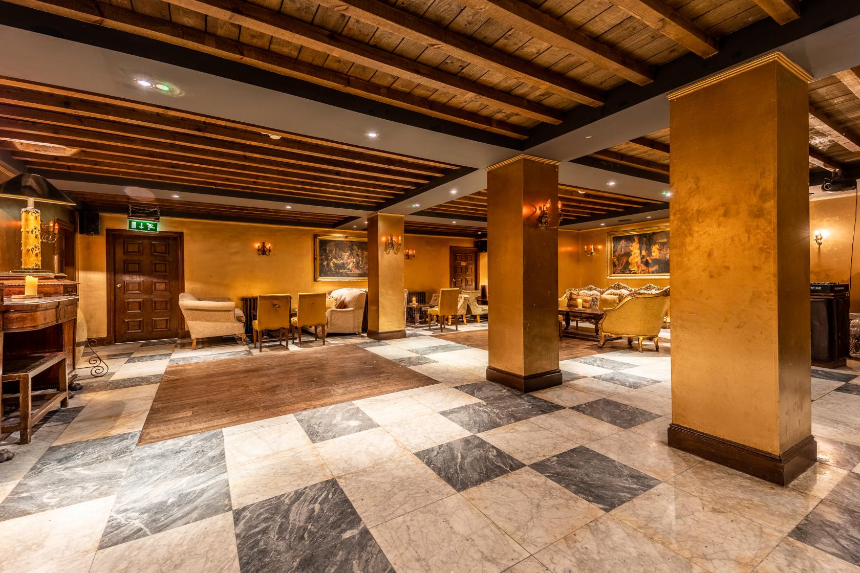 An event space in a restaurant featuring gold walls, exposed wooden beams, and marble flooring at Arta.