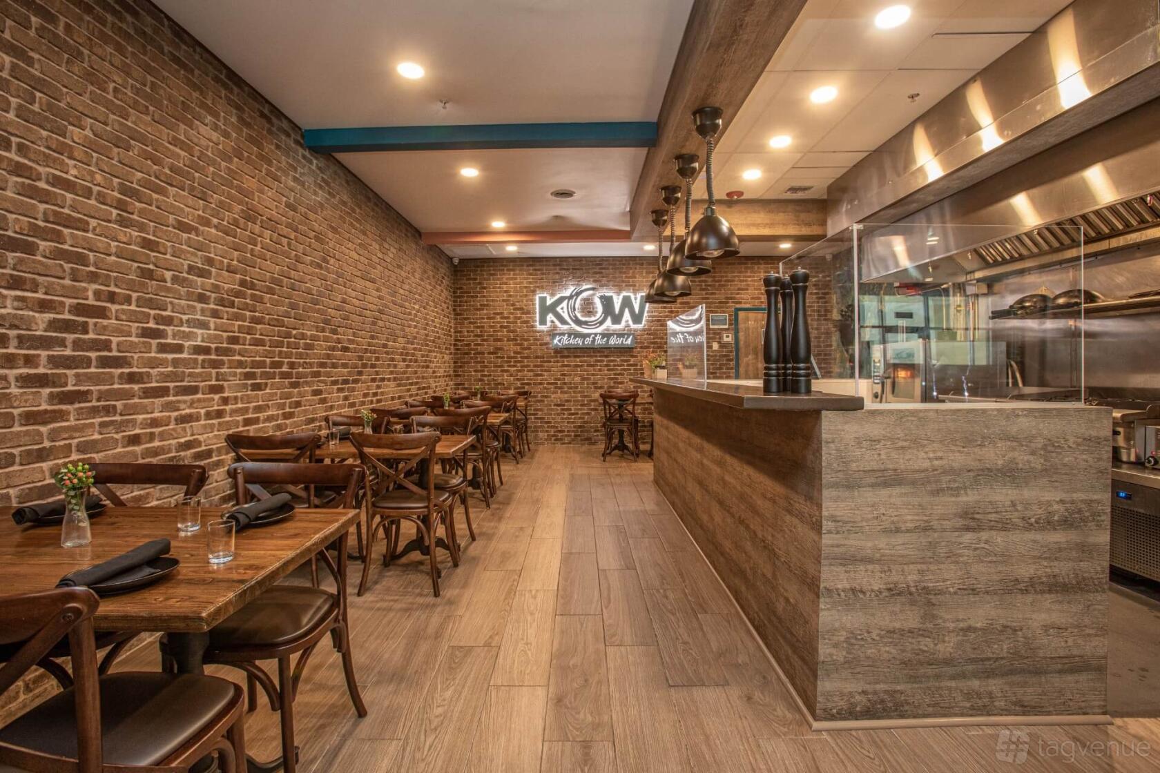 A restaurant with exposed brick walls, wooden tables, and an open kitchen at KOW Restaurant.