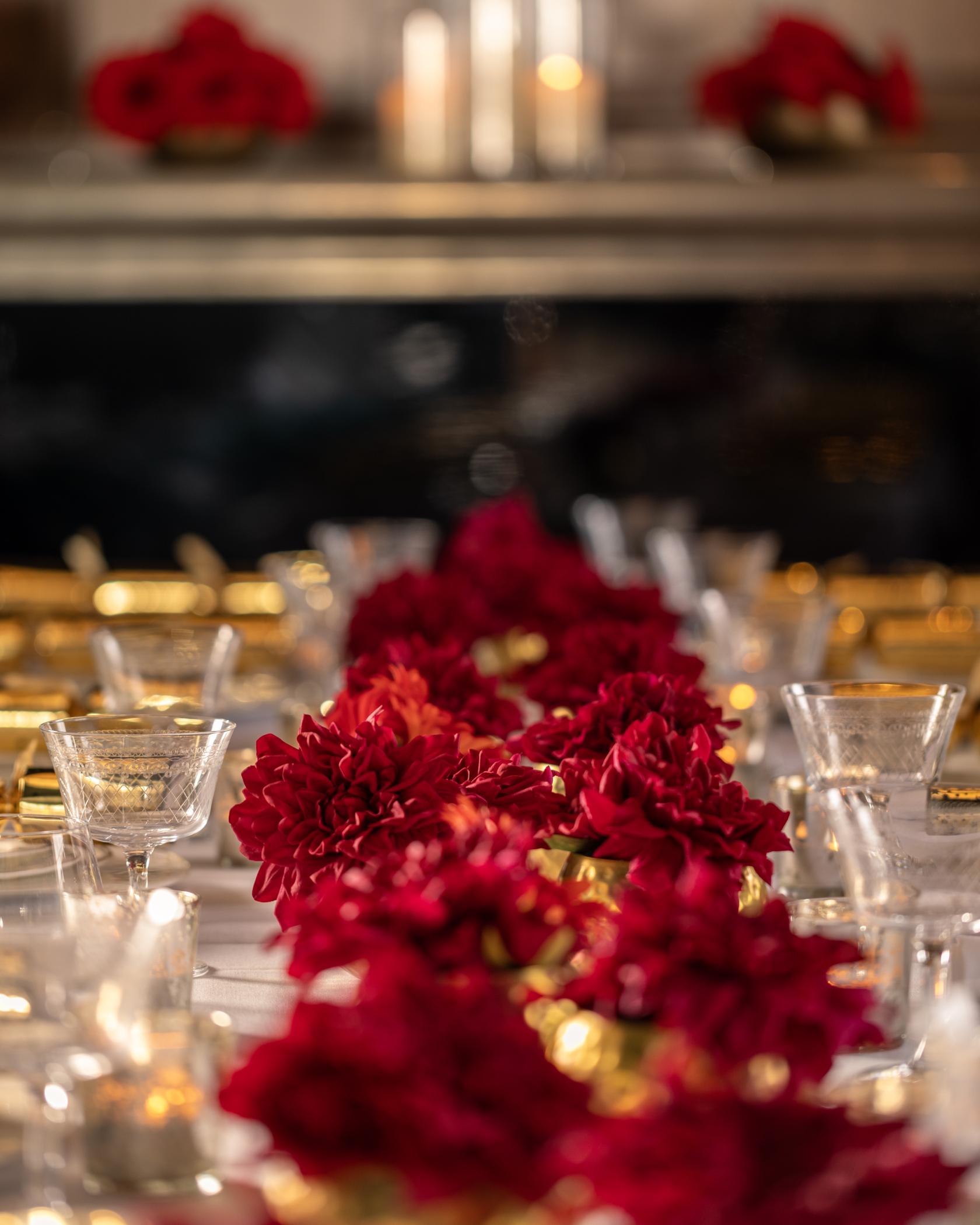 A hotel dining room with red floral centerpieces, gold-rimmed glassware, and elegant table settings at Great Northern Hotel: The Carriage & Lounge.