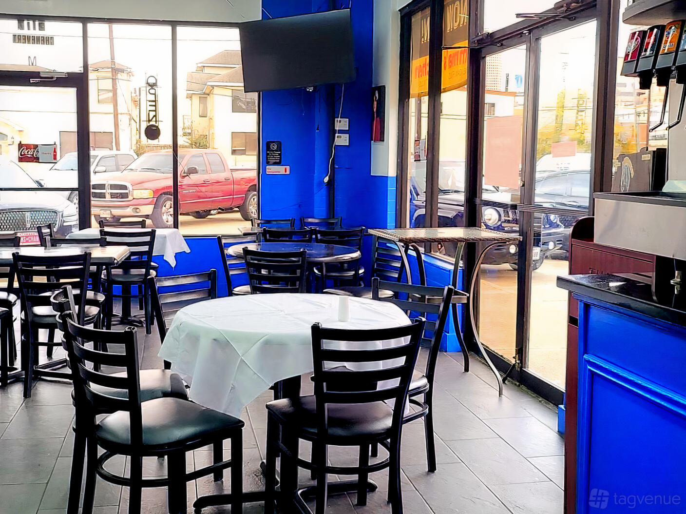 A function room with round tables and black chairs, large windows, and blue walls at Emma's Kitchen.