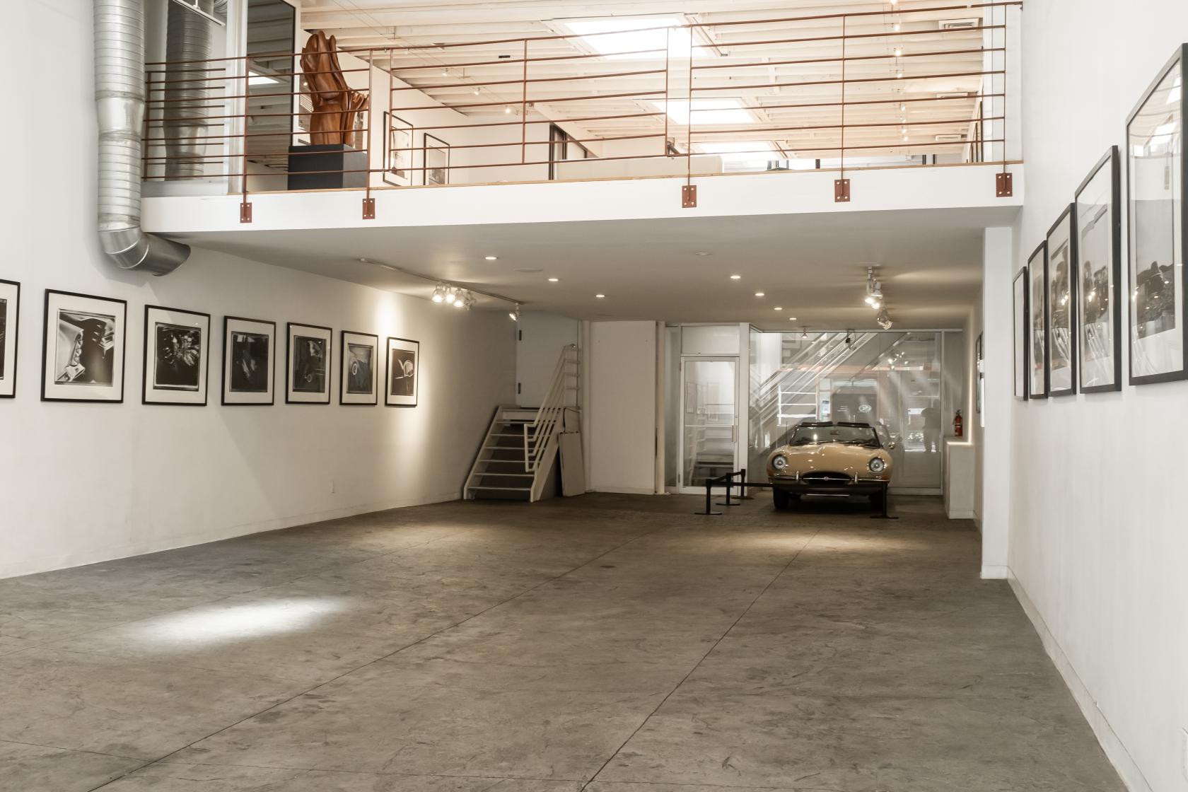 A gallery with framed artwork on white walls, concrete floors, and a visible mezzanine at Cooper Classics Collection.