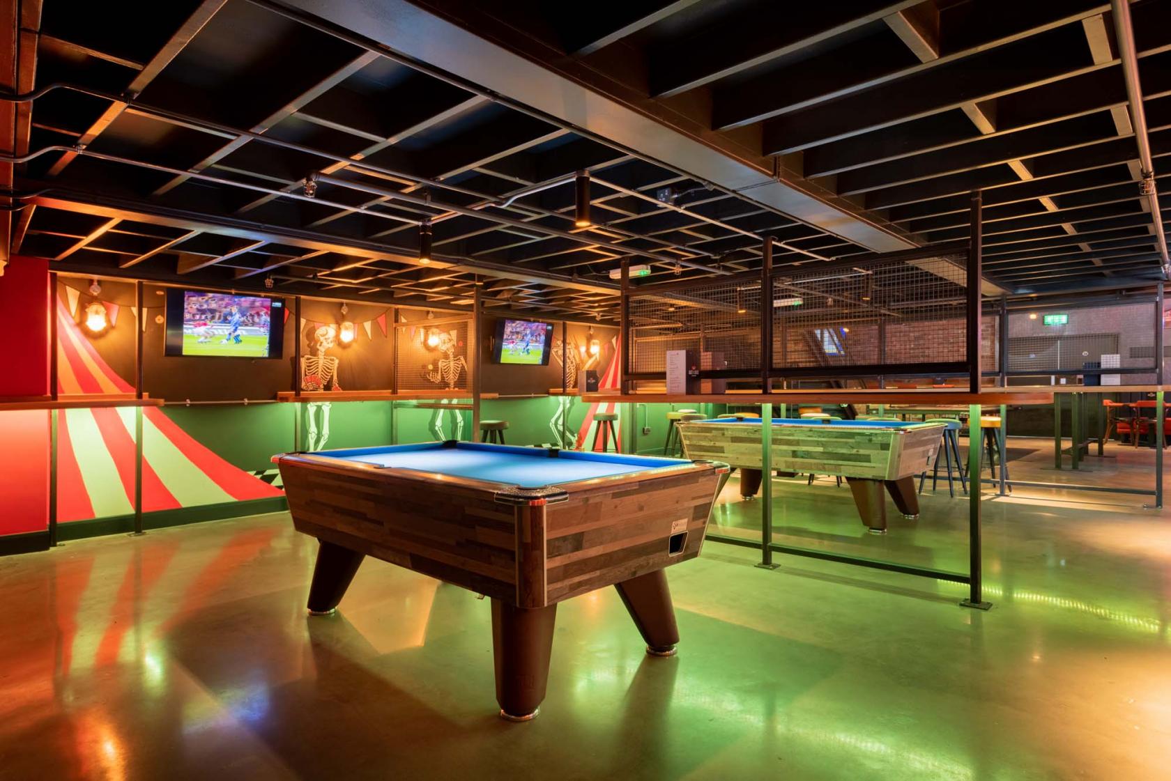 An event space in a bar featuring a pool table, foosball, and neon wall art at Bat & Ball.