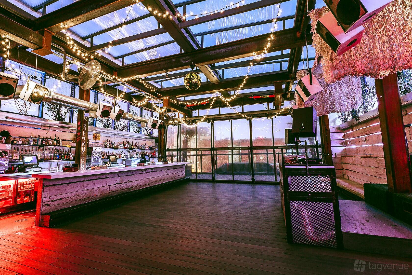 A rooftop nightclub with a glass ceiling, string lights, open bar, and wooden floors at Flash.