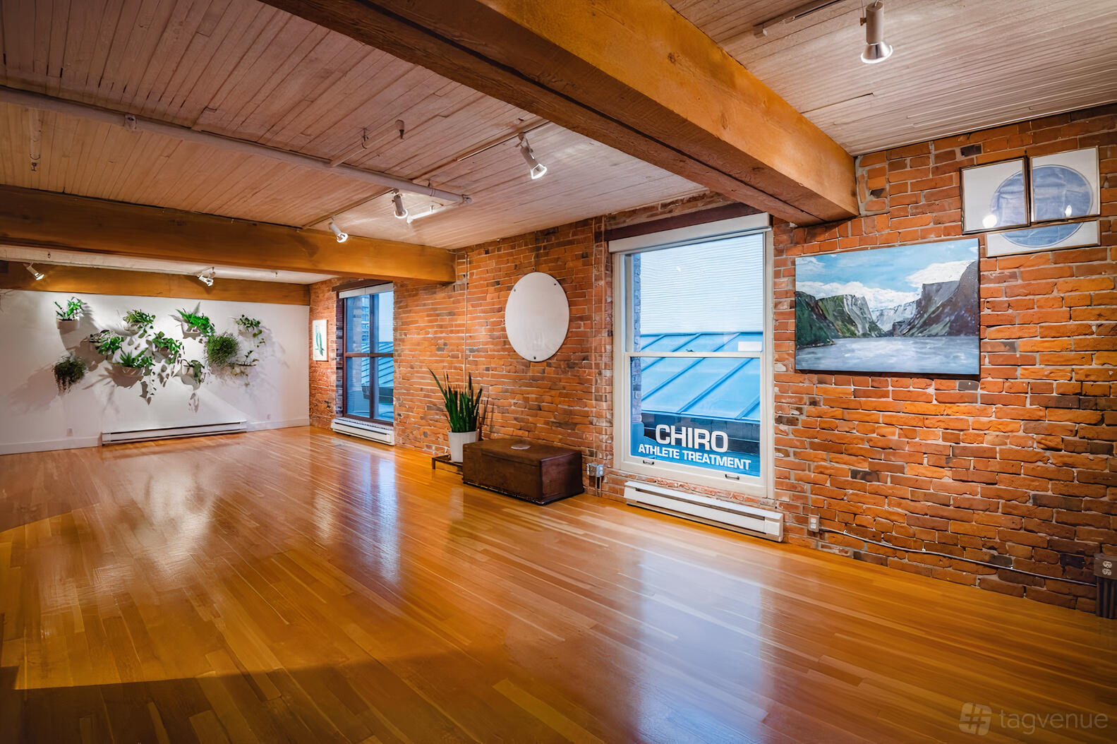 An event venue with exposed brick walls, wood ceiling beams, large windows, and hardwood floors at MVMTLAB.