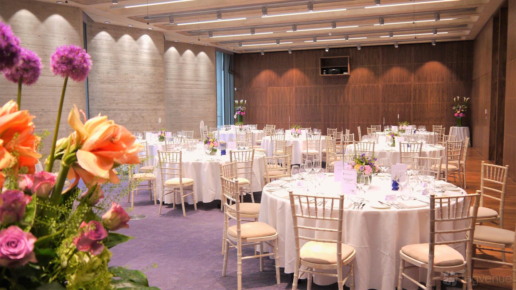 An auditorium with round tables draped in white linens, purple carpet, and wood-paneled walls at Events at No6.