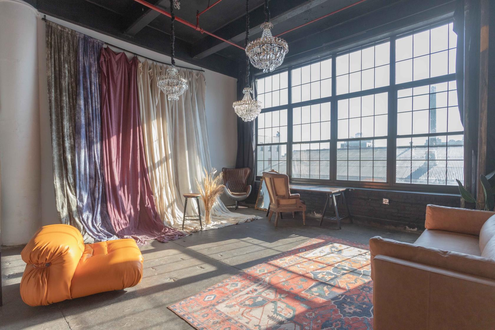 A photo studio with large industrial windows, velvet drapes, chandeliers, and eclectic seating at MikSpace - Stewart Ave.