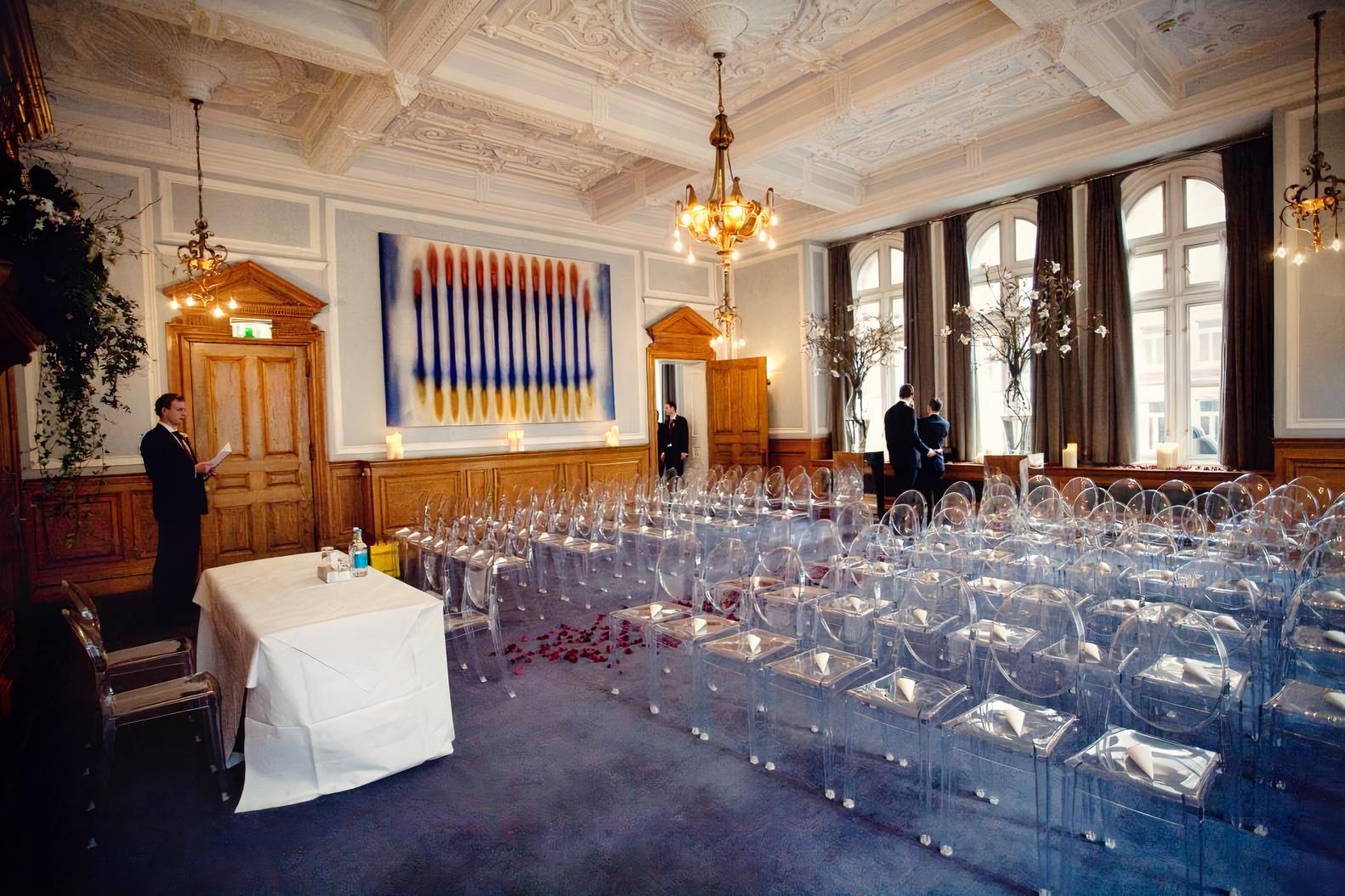 An event space with ornate ceilings, clear chairs, chandeliers, and large arched windows at Andaz London Hotel.